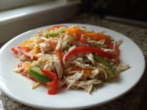 Shredded chicken mixed with colorful strips of red, green, and orange bell peppers, ready for crockpot chicken fajitas.