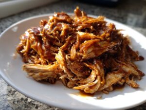 Close-up of shredded crockpot teriyaki chicken coated in rich, glossy sauce served on a white plate.