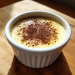 Close-up of a silky egg custard in a white ramekin, topped with sprinkled cinnamon.