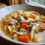 Close-up of a bowl of slow cooker chicken noodle soup with shredded chicken, carrots, and egg noodles.