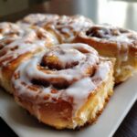 Close-up of several soft, freshly baked cinnamon roll pastries covered in thick white icing.