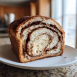 A close-up of a thick slice of sourdough cinnamon bread showing beautiful dark cinnamon swirls in the light dough.