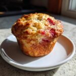 A perfectly baked sourdough strawberry muffin with a golden-brown top, sitting on a small white plate.