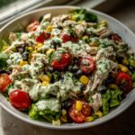 A vibrant bowl of southwest chicken salad featuring shredded chicken, black beans, corn, cherry tomatoes, and a creamy green dressing.