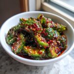 Close-up of a white bowl filled with spicy asian cucumber salad, coated in chili flakes and sesame seeds.