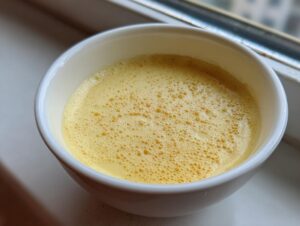 Close-up of smooth, yellow steamed egg custard with small bubbles on top, served in a white bowl.