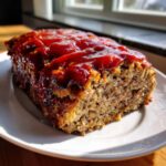 A close-up of a slice of stove top stuffing meatloaf topped with a thick, glossy ketchup glaze.