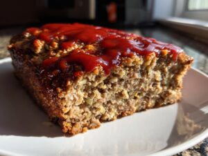 Close-up of a thick slice of stove top stuffing meatloaf topped with a shiny red ketchup glaze.