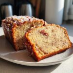 Two slices of moist sweet Alabama pecan bread topped with chopped pecans and powdered sugar on a white plate.
