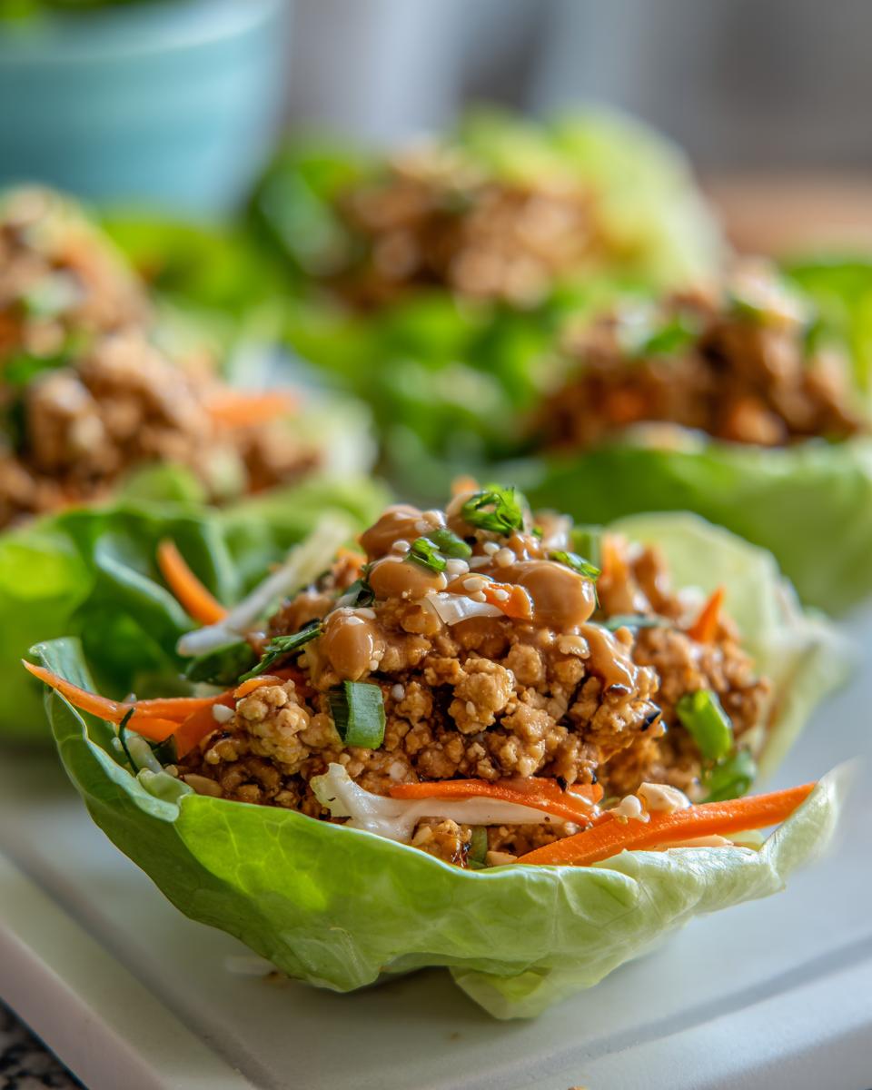 Close-up of a fresh thai peanut chicken lettuce wraps cup filled with savory ground chicken, shredded carrots, and topped with peanut sauce.