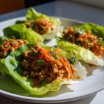 Four servings of thai peanut chicken lettuce wraps filled with ground chicken, shredded carrots, and green onions.