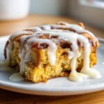 Close-up of a moist slice of tiktok cinnamon roll casserole generously drizzled with white cream cheese icing.