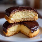 Close-up of two vanilla wafer boston cream pie cookies stacked, showing the creamy filling and chocolate glaze.