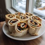 Eight slices of vegan taco pinwheels filled with black beans and vegetables arranged on a white plate.