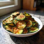 A white bowl overflowing with crispy, seasoned air fryer zucchini chips, catching the sunlight.
