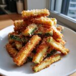 A pile of crispy, golden-brown air fryer zucchini with parmesan sticks served on a white plate.