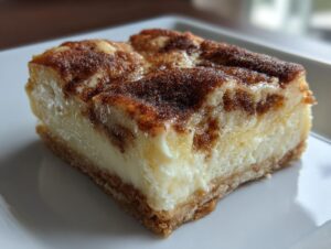 Close-up of a square slice of brown butter cream cheese snickerdoodle cobbler on a white plate.