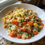 A close-up of a white bowl filled with colorful cauliflower fried rice, featuring bright orange carrots and green peas.