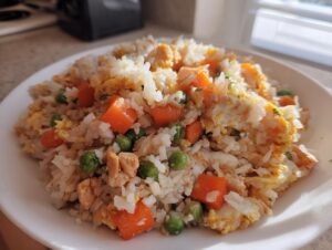 Close-up of a white plate filled with homemade cauliflower fried rice mixed with scrambled egg, diced carrots, and green peas.