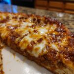 A close-up shot of a thick slice of pizza featuring a rich, meaty topping and melted mozzarella cheese on a carnivore pizza crust.