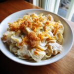 A close-up of a serving of creamy chicken noodle casserole topped with melted cheddar cheese and crunchy breadcrumbs.