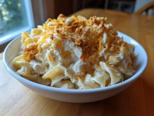 A bowl of creamy chicken noodle casserole topped with golden breadcrumbs and shredded cheddar cheese.