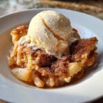 A warm serving of crockpot snickerdoodle cobbler topped with a melting scoop of vanilla ice cream and cinnamon sugar.