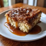 A close-up of a square slice of warm snickerdoodle cobbler topped with cinnamon sugar and drizzled with rich caramel sauce.
