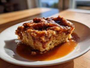 A close-up of a warm slice of snickerdoodle cobbler drenched in gooey caramel sauce on a white plate.