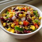 Close-up of a white bowl filled with high protein cowboy caviar recipe featuring quinoa, black beans, corn, and diced peppers.
