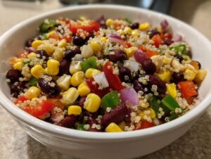 Close-up of a white bowl filled with vibrant high protein cowboy caviar recipe featuring quinoa, black beans, corn, and chopped peppers.