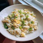 A white bowl filled with keto cauliflower fried rice mixed with scrambled egg pieces and topped with sliced green onions.