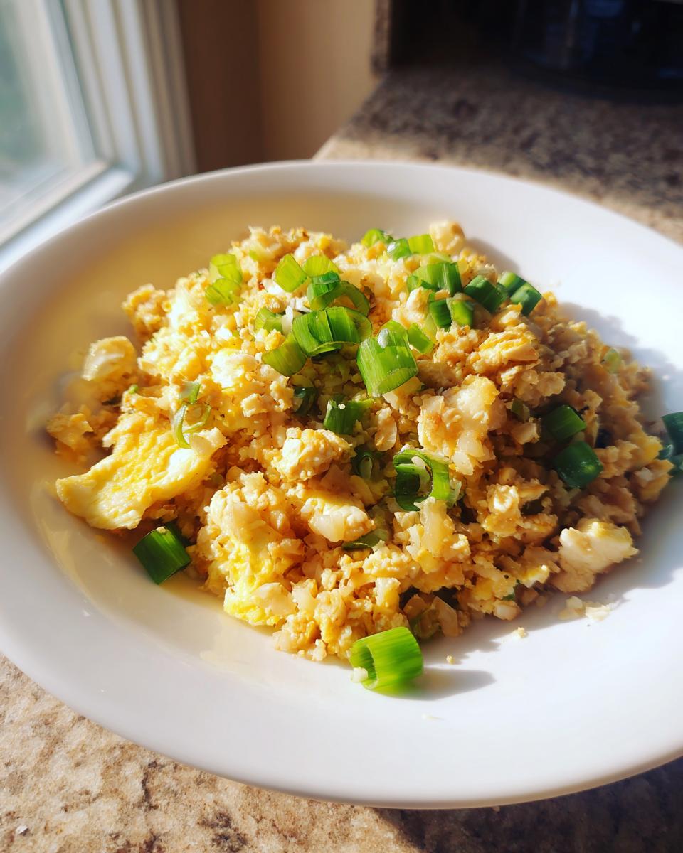 A white bowl filled with bright yellow keto cauliflower fried rice, topped generously with chopped green onions.