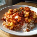 A close-up of kimchi cauliflower fried rice served over white rice in a light bowl, garnished with herbs.