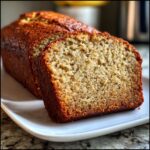 Close-up of a sliced loaf of moist cottage cheese banana bread on a white plate.