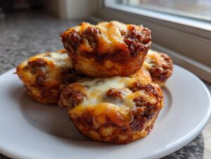Four baked muffin-tin carnivore pizza bites topped with browned meat filling and melted mozzarella cheese on a white plate.